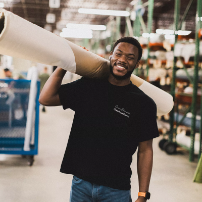 A man smiling carrying a large roll of fabric over his shoulder