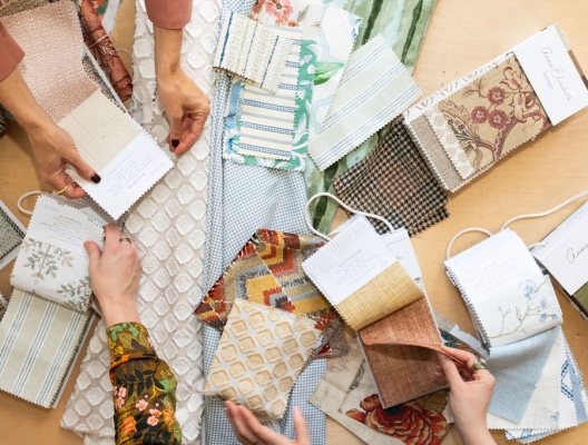 Two pairs of hands and lots of fabric swatches on a wood table